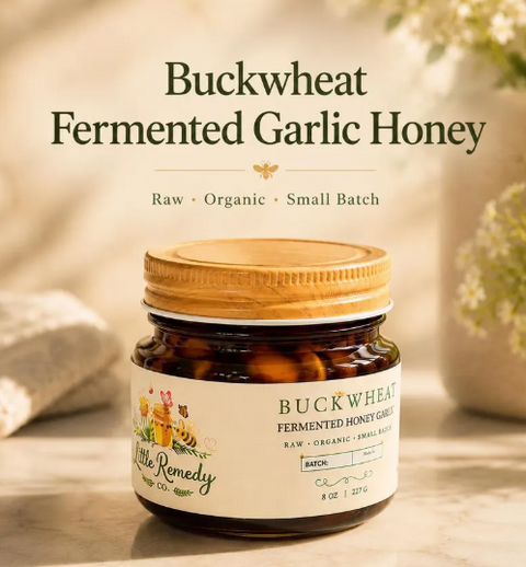 A jar of Buckwheat Fermented Garlic Honey by Little Remedy Co. is shown on a light stone surface with a soft, warm background.