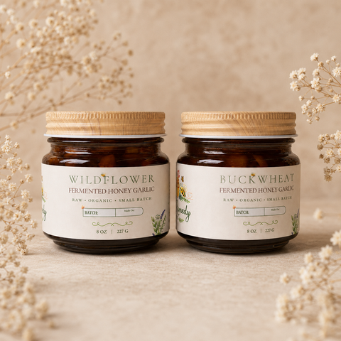 Two jars of Wildflower and Buckwheat Fermented Honey Garlic on a neutral background with flowers.