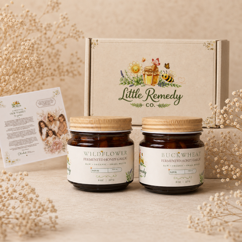 Two jars of 'Little Remedy Co.' fermented honey garlic on a beige surface with a branded box in the background.